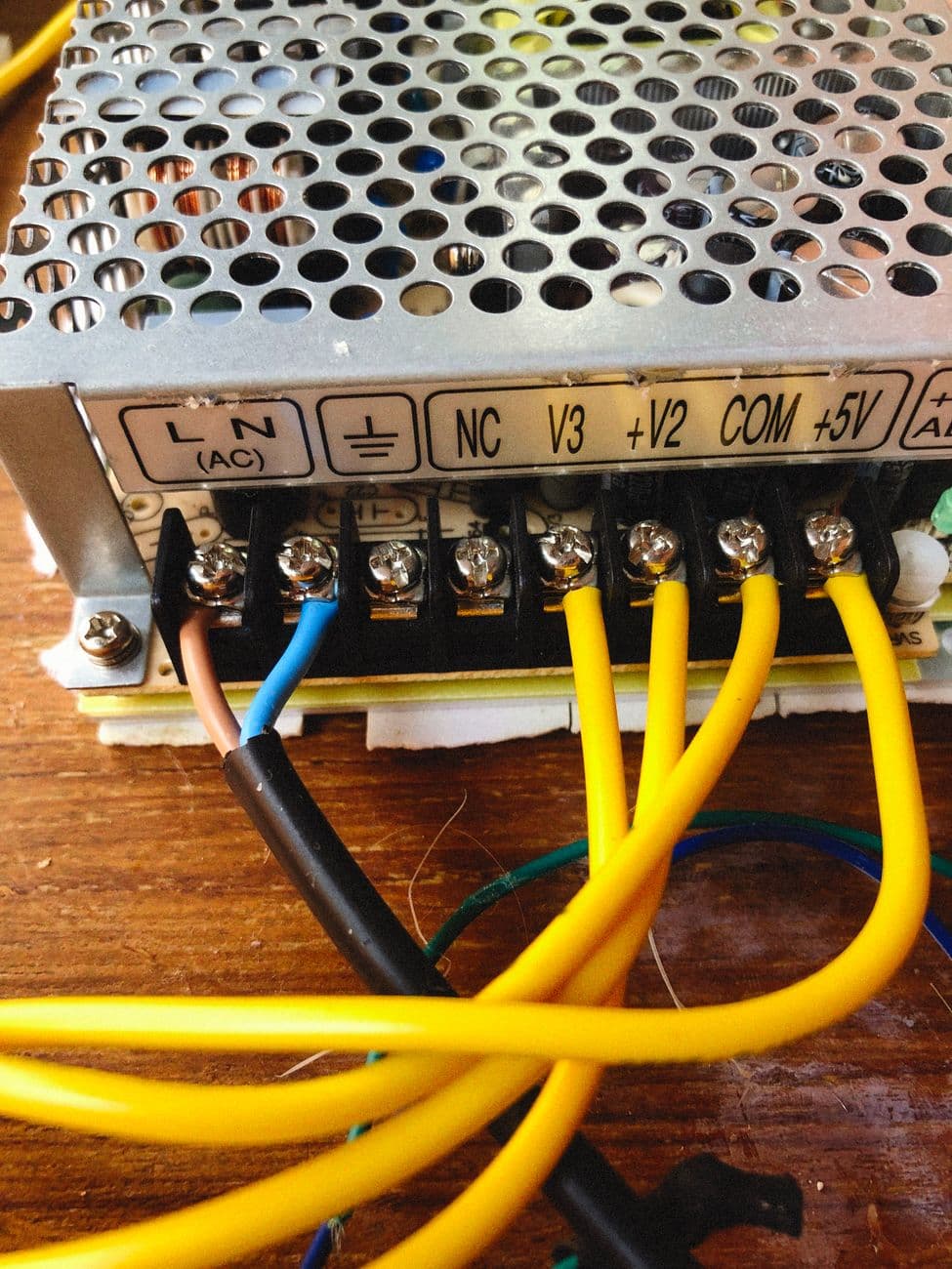 Conductors landed in a row of screw terminals on a power supply, with the terminals labelled.