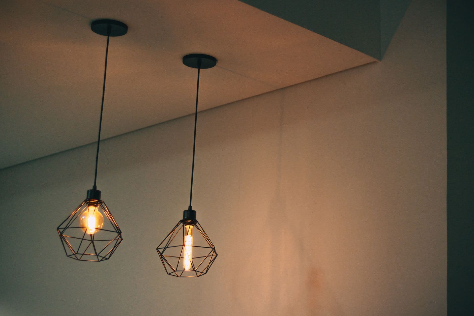 Two pendant lights with wire cage shades hanging from a ceiling.