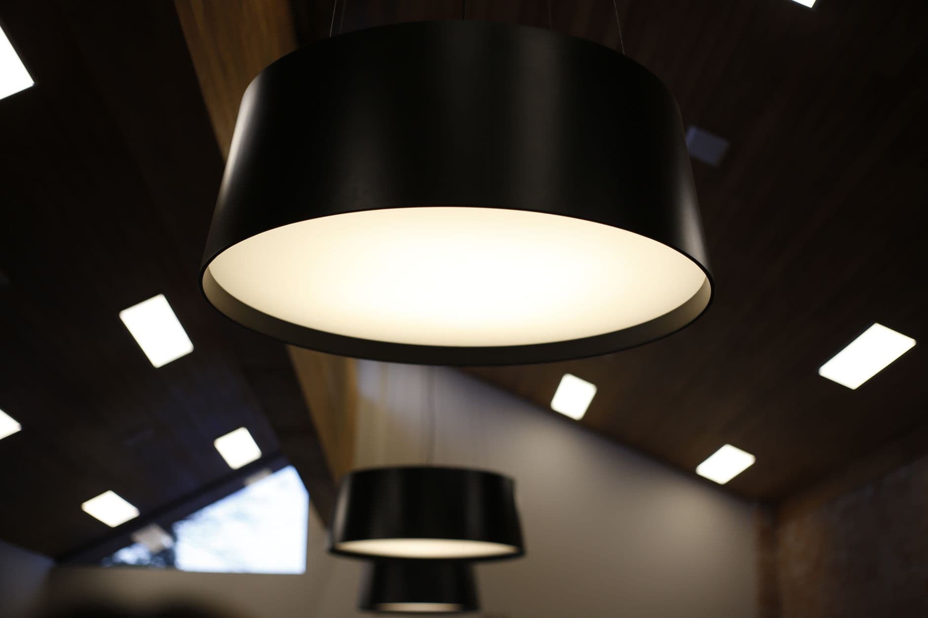 A large drum pendant light below a ceiling with recessed square lights.