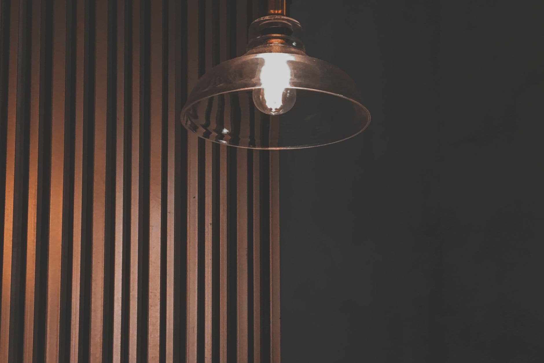 A glass pendant light lit in front of a timber-slatted wall.