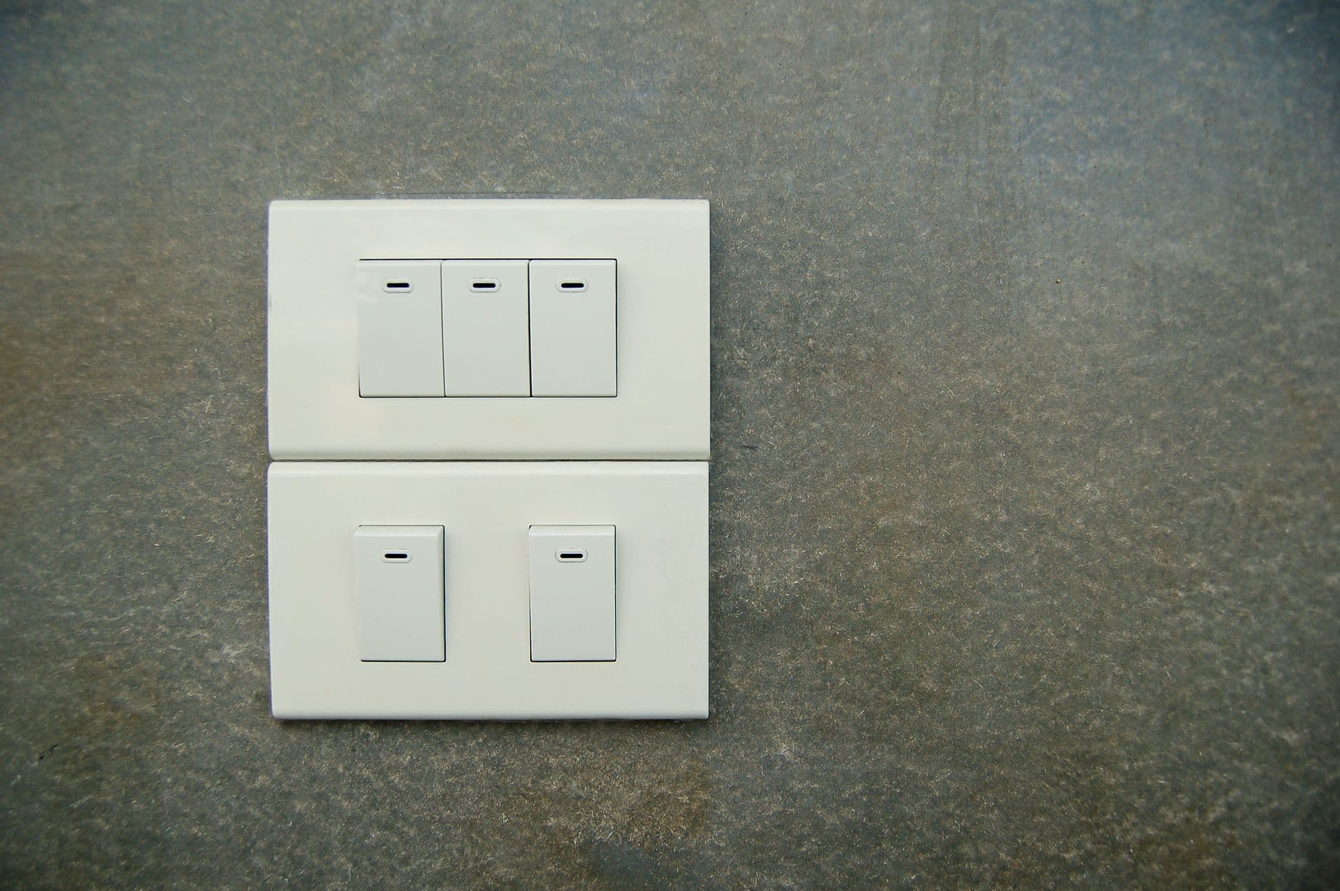 Two white rocker switch plates on a textured stone wall.
