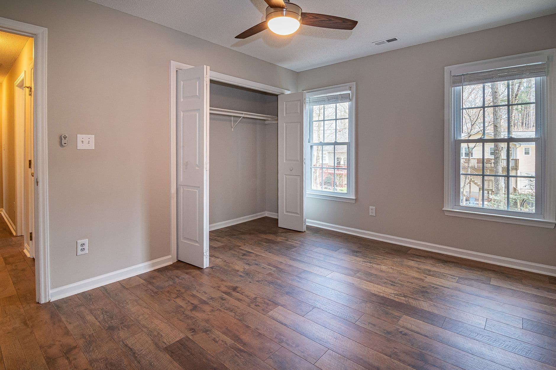 An empty room with a ceiling fan, a light switch beside the door and timber flooring.