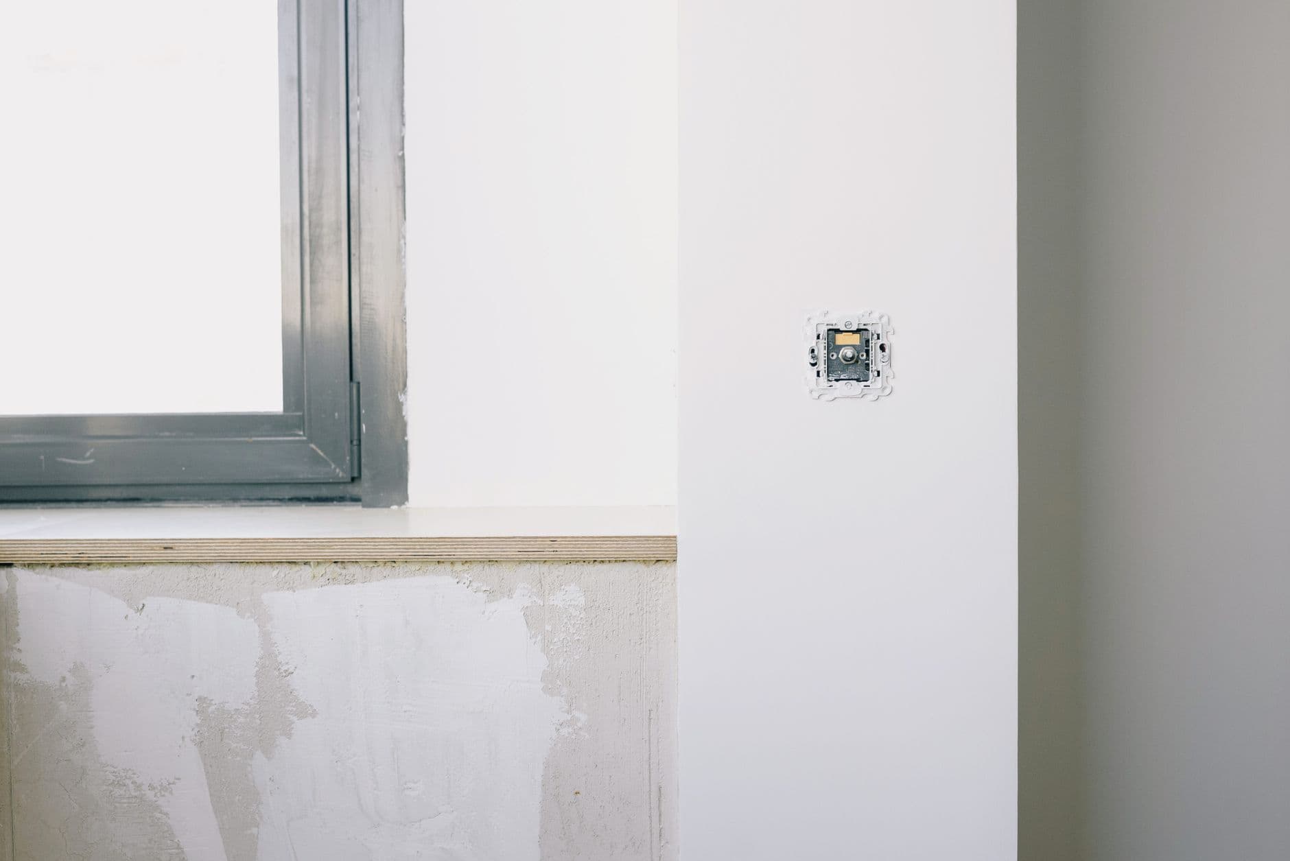 A new socket back box set into a freshly plastered wall beside a window frame.